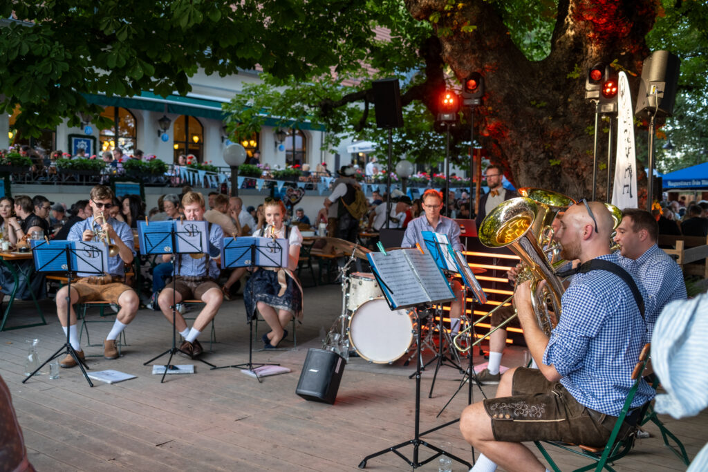 Auftritt im Biergarten im Zollpackhof unter einer alten Kastanie: die Band sitzt in Karohemden und Lederhosen an den Notenständern, ringsum besetzte Bierbänke.